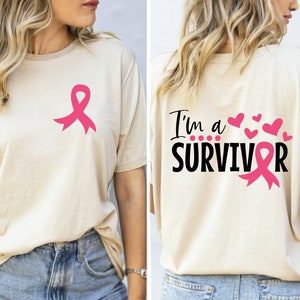 A beige shirt with a pink ribbon on the left side and the text 'I'm a SURVIVOR' with a pink ribbon on the right side.