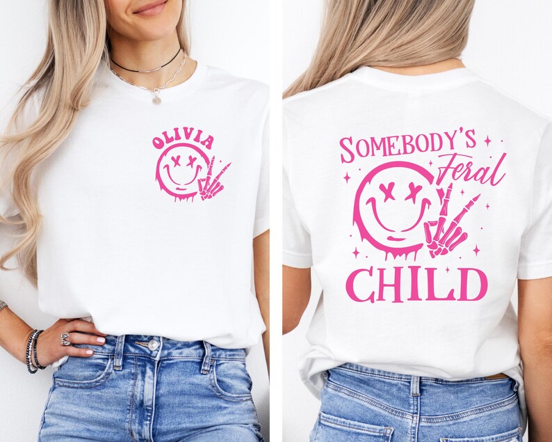 May include: White t-shirt with a pink smiley face with crossed eyes and a skeleton hand making a peace sign. The text "Olivia" is above the smiley face. The back of the shirt has a pink smiley face with crossed eyes and a skeleton hand making a peace sign. The text "Somebody's Feral Child" is above the smiley face.