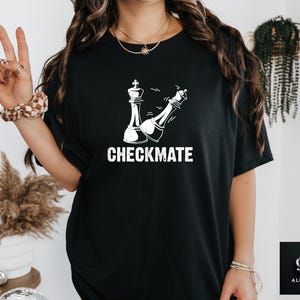 May include: Black t-shirt with a white graphic of two chess pieces in a checkmate position. The text "CHECKMATE" is printed below the chess pieces.