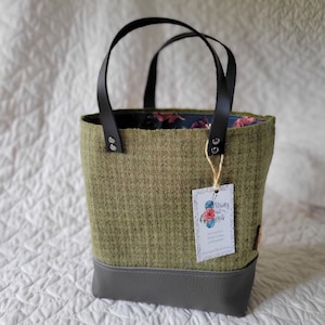May include: A green and gray tote bag with black handles. The bag has a floral lining and a leather bottom. A tag is attached to the bag that says "Strung out on Knits".
