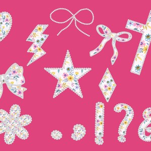 May include: A collection of floral-patterned embellishments on a pink background. The designs include a heart, lightning bolt, star, bow, cross, flower, diamond, punctuation marks, and a bow made of pearls. The floral patterns feature yellow, blue, and purple flowers.
