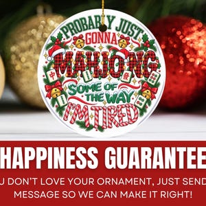 Puede incluir: Un adorno navide&ntilde;o redondo de cer&aacute;mica blanca con el texto MAHJONG en un patr&oacute;n de cuadros rojos y negros. La frase dice PROBABLY JUST GONNA MAHJONG SOME OF THE WAY I'M TIRED, rodeada de ramas de pino verdes, lazos rojos, campanas doradas y fichas de mahjong.