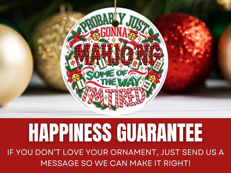 Puede incluir: Un adorno navide&ntilde;o redondo de cer&aacute;mica blanca con el texto MAHJONG en un patr&oacute;n de cuadros rojos y negros. La frase dice PROBABLY JUST GONNA MAHJONG SOME OF THE WAY I'M TIRED, rodeada de ramas de pino verdes, lazos rojos, campanas doradas y fichas de mahjong.
