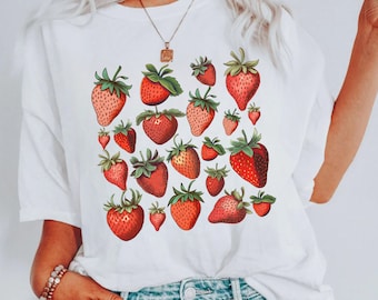 May include: White t-shirt with a red and green strawberry print. The strawberries are arranged in a random pattern across the shirt.