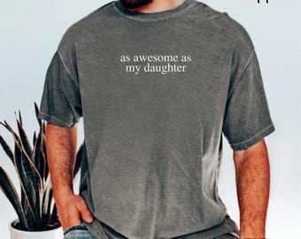 May include: A dark gray t-shirt with the text "as awesome as my daughter" printed on the front.