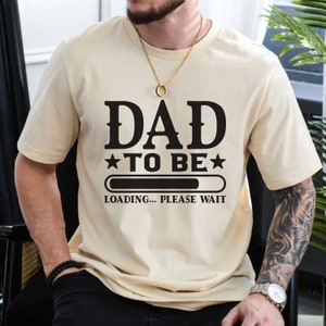 May include: A beige t-shirt with black text that reads "DAD TO BE" with a progress bar that says "LOADING... PLEASE WAIT".