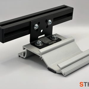 以下が含まれることがあります： 黒い金属製のブラケットと銀色の金属製のベース。ブラケットには2本のネジと金属製のプレートが付いています。ベースには溝とゴム製のストリップがあります。