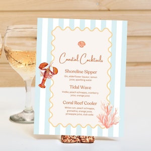May include: A blue and white striped card with a gold border and a seashell design. The card has the text "Coastal Cocktails" and lists three cocktails: Shoreline Sipper, Tidal Wave, and Coral Reef Cooler. The card is sitting on a white surface with two glasses of white wine.