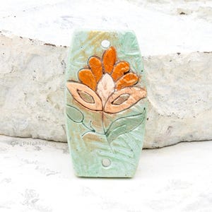 May include: A ceramic tile with a raised floral design. The flower is orange and white with green leaves on a light green background.