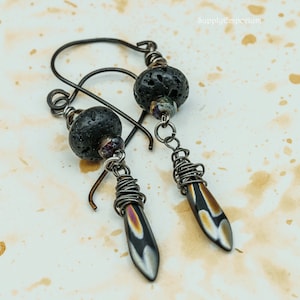 May include: A pair of earrings with black lava rock beads and silver wire wrapped teardrop shaped pendants with iridescent glass accents.