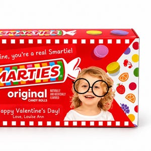 May include: A rectangular red box of Smarties original candy rolls, net weight 85 g. The packaging features colourful candy illustrations, the text "Valentine, you're a real Smartie!", "Happy Valentine's Day!", and a child wearing black-rimmed glasses.