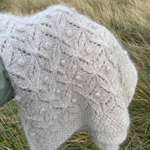 May include: A light gray knitted shawl with a delicate lace pattern and pearl embellishments.