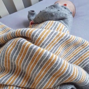 May include: A baby is swaddled in a striped knitted blanket with yellow and gray stripes. The blanket is soft and cozy, perfect for keeping a baby warm and comfortable.
