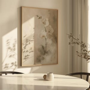 K&ouml;nnte beinhalten: Ein rechteckiges Wandbild in einem hellen Holzrahmen mit einem Gem&auml;lde in weichen, neutralen T&ouml;nen, das einen wei&szlig;en Orchideenzweig zeigt. Das Kunstwerk pr&auml;sentiert zarte Bl&uuml;tenbl&auml;tter vor einem ged&auml;mpften, strukturierten beigen Hintergrund.