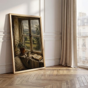 May include: A framed print of a window scene. The artwork depicts a window with a view of a green landscape, a potted plant, a cup, and an open book. The frame is light-colored, and the artwork is leaning against a white wall.