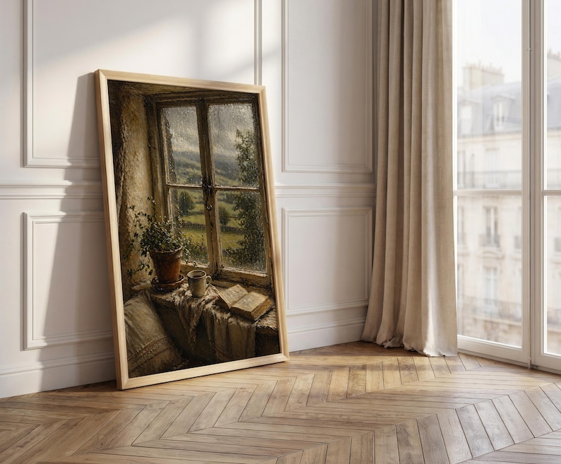 May include: A framed print of a window scene. The artwork depicts a window with a view of a green landscape, a potted plant, a cup, and an open book. The frame is light-colored, and the artwork is leaning against a white wall.