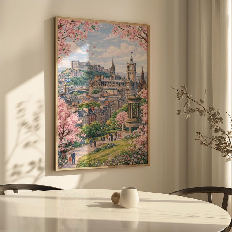 May include: A framed print of a cityscape, featuring a castle and buildings, framed by pink flowering trees. The artwork has a light wood frame and is hanging on a white wall. The scene is a watercolor painting with a soft, pastel color palette.