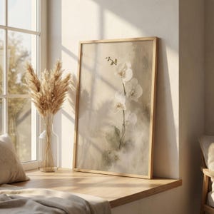 K&ouml;nnte beinhalten: Ein rechteckiger gerahmter Wandkunstdruck mit einem zarten wei&szlig;en Orchideenzweig vor einem weichen, strukturierten beigen und cremefarbenen Hintergrund. Das Kunstwerk ist in einem hellen Holzrahmen gefasst und zeigt eine botanische Illustration mit feinen Pinselstrichen.