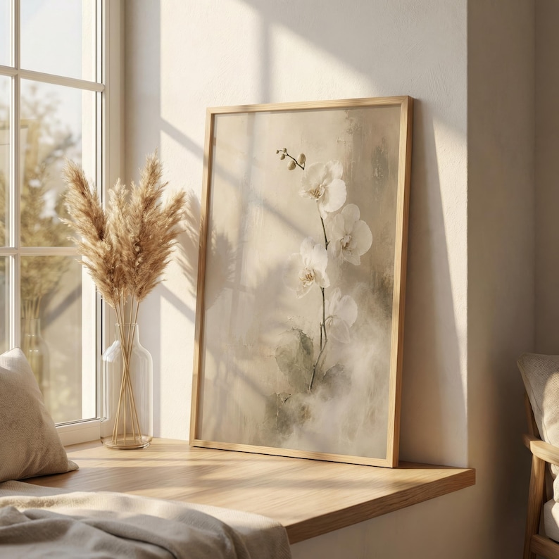 K&ouml;nnte beinhalten: Ein rechteckiger gerahmter Wandkunstdruck mit einem zarten wei&szlig;en Orchideenzweig vor einem weichen, strukturierten beigen und cremefarbenen Hintergrund. Das Kunstwerk ist in einem hellen Holzrahmen gefasst und zeigt eine botanische Illustration mit feinen Pinselstrichen.