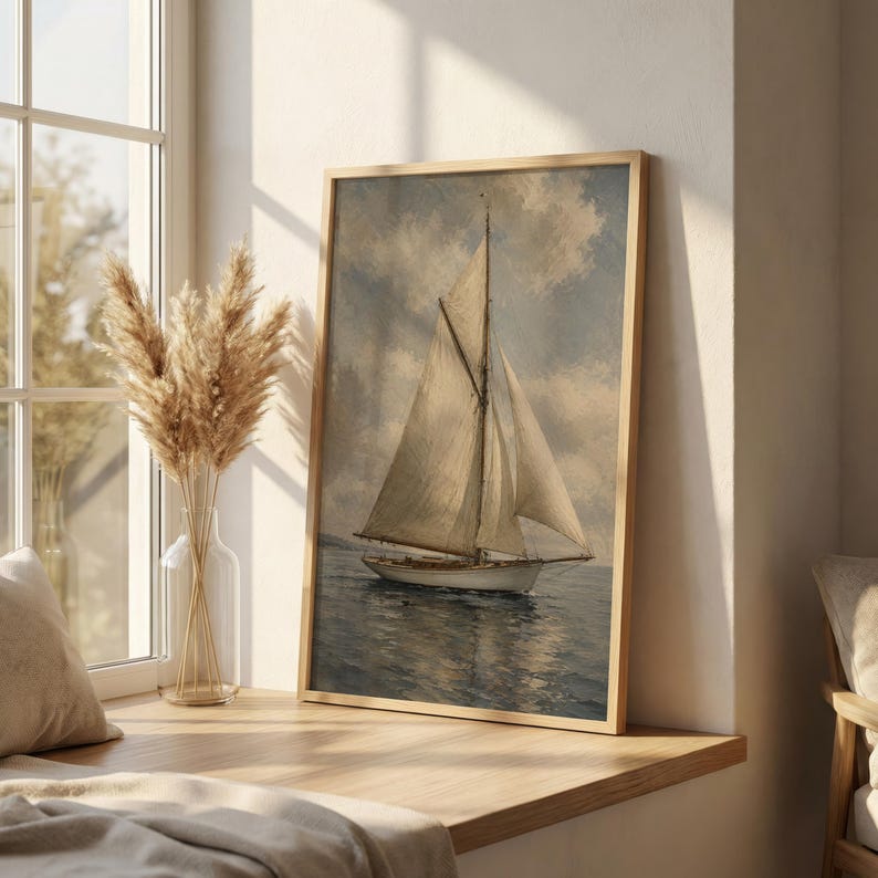May include: A framed nautical print depicts a sailboat on the water under a cloudy sky. The sailboat has white sails and a wooden hull. The artwork is in a light wooden frame and is displayed near a window with dried flowers in a vase.