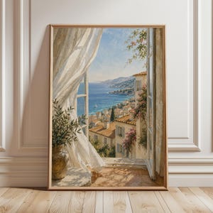 May include: A framed watercolour painting showing a coastal European town through an open window. The scene includes a blue sea, white curtains, and terracotta rooftops. A vase with greenery sits on the windowsill. The artwork is in a wooden frame.