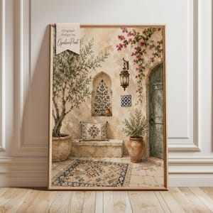 May include: A framed wall art print featuring a Mediterranean courtyard scene with an olive tree in a stone pot, a patterned throw pillow on a stone bench, a hanging lantern, a blue arched door, and pink bougainvillea flowers.