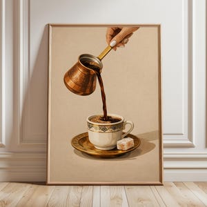 May include: Framed print of coffee being poured from a copper cezve into a white teacup with a gold saucer. The cup and saucer have a gold and blue design. A piece of Turkish delight sits on the saucer.