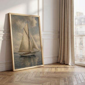 May include: A framed vintage painting of a sailboat on the water. The artwork features a light-colored sailboat with white sails against a cloudy sky. The frame is a light wood color, and the painting is leaning against a white wall.