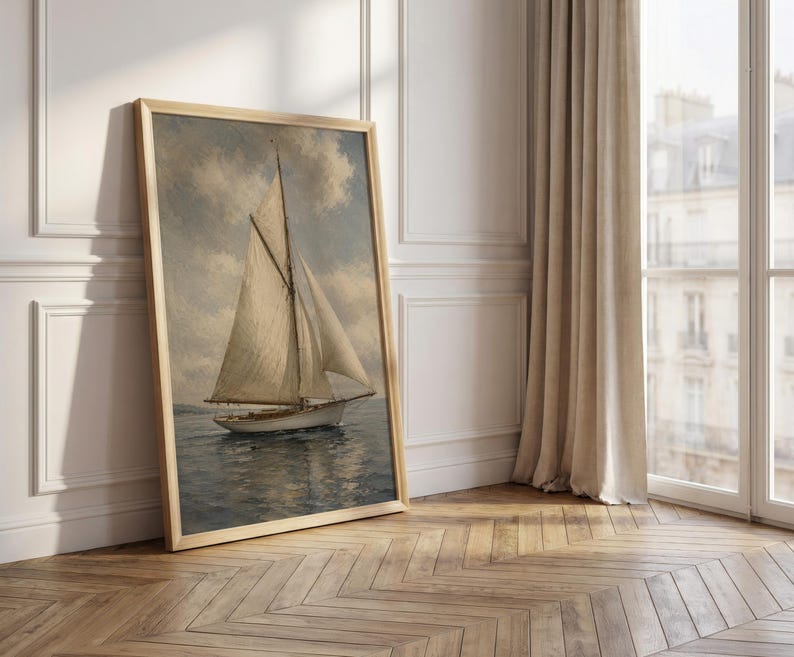 May include: A framed vintage painting of a sailboat on the water. The artwork features a light-colored sailboat with white sails against a cloudy sky. The frame is a light wood color, and the painting is leaning against a white wall.