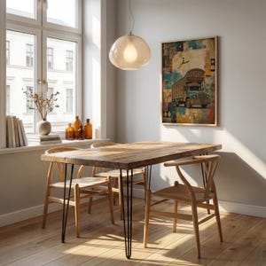 Op de afbeelding: Een rechthoekige houten eettafel met dunne zwarte metalen haarspeldpoten, vergezeld door drie lichtgekleurde houten stoelen met gevlochten zittingen. Een ingelijste kunstdruk van een versierde vrachtwagen met Arabische tekst hangt aan de muur.