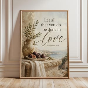 May include: A framed wall art print featuring a Mediterranean landscape with a stone ledge, a rustic ceramic vase with olive branches, and a bowl of fresh figs. The text reads: Let all that you do be done in love, 1 Corinthians 16:14.