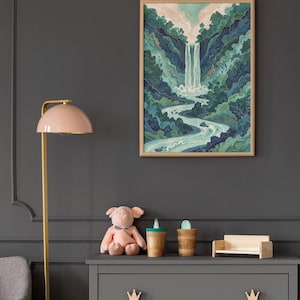 May include: A framed watercolor print of a waterfall cascading into a river, surrounded by lush green and blue foliage. The artwork hangs on a dark gray wall above a gray dresser with wooden crown-shaped drawer pulls. A pink lamp and stuffed pig are also visible.