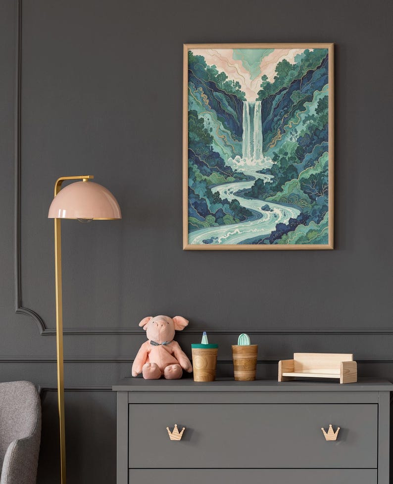 May include: A framed watercolor print of a waterfall cascading into a river, surrounded by lush green and blue foliage. The artwork hangs on a dark gray wall above a gray dresser with wooden crown-shaped drawer pulls. A pink lamp and stuffed pig are also visible.