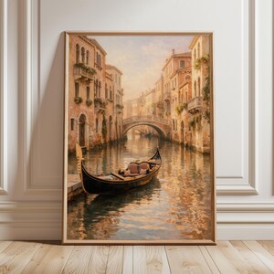 Peut inclure: Une impression d'art encadrée représentant une scène de canal vénitien. L'œuvre présente une gondole, des bâtiments avec balcons, un pont et des reflets dans l'eau. La palette de couleurs comprend des tons chauds de beige, de brun et d'or.
