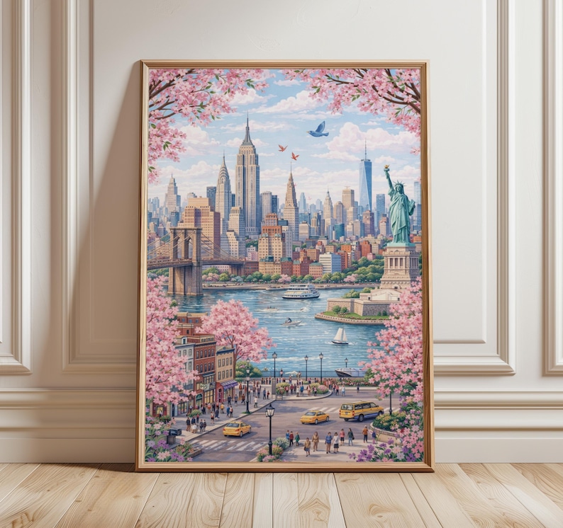 Op de afbeelding: Een ingelijste kunstdruk met een levendige sc&egrave;ne van New York City. Het kunstwerk toont de skyline, inclusief het Empire State Building en het Vrijheidsbeeld, omlijst door bloeiende roze kersenbloesems. Gele taxi's en een brug zijn ook zichtbaar.