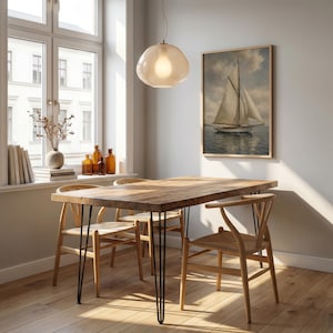 May include: A dining room scene featuring a wooden table with black hairpin legs and four wooden chairs. A framed painting of a sailboat hangs on the wall. A light fixture hangs above the table, and a window with a view is visible.
