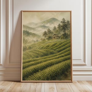 Puede incluir: Pintura en acuarela enmarcada de una plantación de té en un paisaje montañoso y brumoso. La obra presenta campos de té verdes ondulados, una pequeña casa tradicional y montañas distantes. La pintura está en un marco de madera.