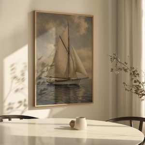 May include: A framed nautical art print depicts a sailboat on the water under a cloudy sky. The artwork features a vintage aesthetic with muted tones of beige, blue, and brown. The print is displayed in a light wood frame.