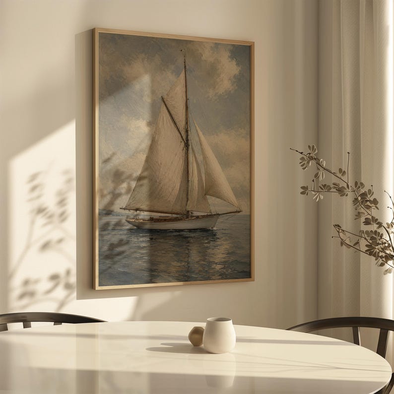 May include: A framed nautical art print depicts a sailboat on the water under a cloudy sky. The artwork features a vintage aesthetic with muted tones of beige, blue, and brown. The print is displayed in a light wood frame.