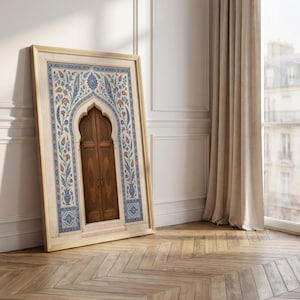 Puede incluir: Una obra de arte enmarcada que presenta una puerta de madera con una parte superior arqueada, enmarcada en un borde decorativo de patrones florales azules, naranjas y blancos. La obra de arte est&aacute; apoyada contra una pared blanca, con un suelo de madera en primer plano.