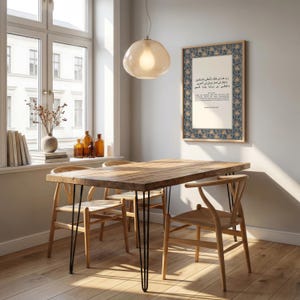 May include: A dining room scene featuring a wooden table with black hairpin legs and four wooden chairs. A framed print with Arabic text hangs on the wall. A glass pendant light hangs above the table. Decorative items are on the windowsill.
