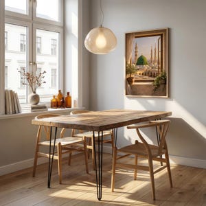 May include: A dining room scene featuring a wooden table with black hairpin legs and four wooden chairs. A framed artwork depicting a Middle Eastern cityscape hangs on the wall. A large window and a pendant light complete the room's decor.
