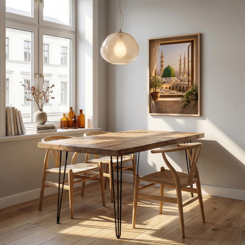 May include: A dining room scene featuring a wooden table with black hairpin legs and four wooden chairs. A framed artwork depicting a Middle Eastern cityscape hangs on the wall. A large window and a pendant light complete the room's decor.