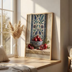 May include: A framed print featuring a still life with pomegranates. A decorative bowl filled with ripe pomegranates sits on a stone ledge. The background includes a patterned tile design in blue, green, and white, with a wooden frame.