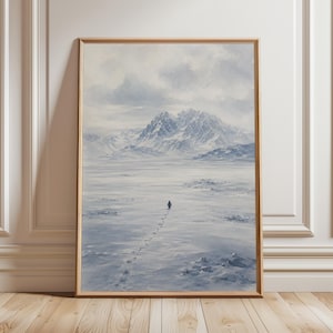 May include: A vertical rectangular wall art print in a light wood frame featuring a watercolour painting of a lone penguin walking across a vast, snow-covered landscape towards distant, jagged, snow-capped mountains under a cloudy, pale sky.