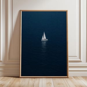 May include: A framed print featuring a sailboat on a deep blue ocean. The white sailboat is centered, with its sails catching the light. The artwork is in a wooden frame, set against a white wall and wooden floor.