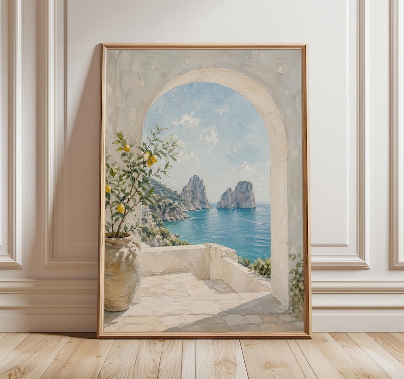 May include: Framed art print of a coastal scene. The painting depicts a white arched doorway overlooking a turquoise sea with rock formations. A potted lemon tree with yellow fruit sits on a white terrace. The artwork is in a wooden frame.