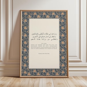 May include: Framed art print featuring Arabic calligraphy and English text. The artwork has a cream-colored background with text in both languages. The frame is gold, and the border has a blue and gold floral pattern. The print is displayed on a wooden floor.