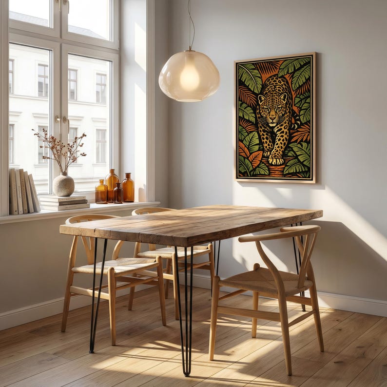 May include: A dining room scene featuring a wooden table with black hairpin legs and four wooden chairs. A framed artwork of a jaguar in a jungle setting hangs on the wall. A light fixture hangs above the table, and a window is visible.