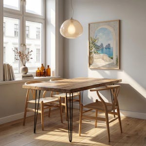 May include: A rustic wooden dining table with black hairpin legs and four wooden chairs. A light fixture hangs above the table. A framed painting of a coastal scene hangs on the wall. The room has a window with a view.